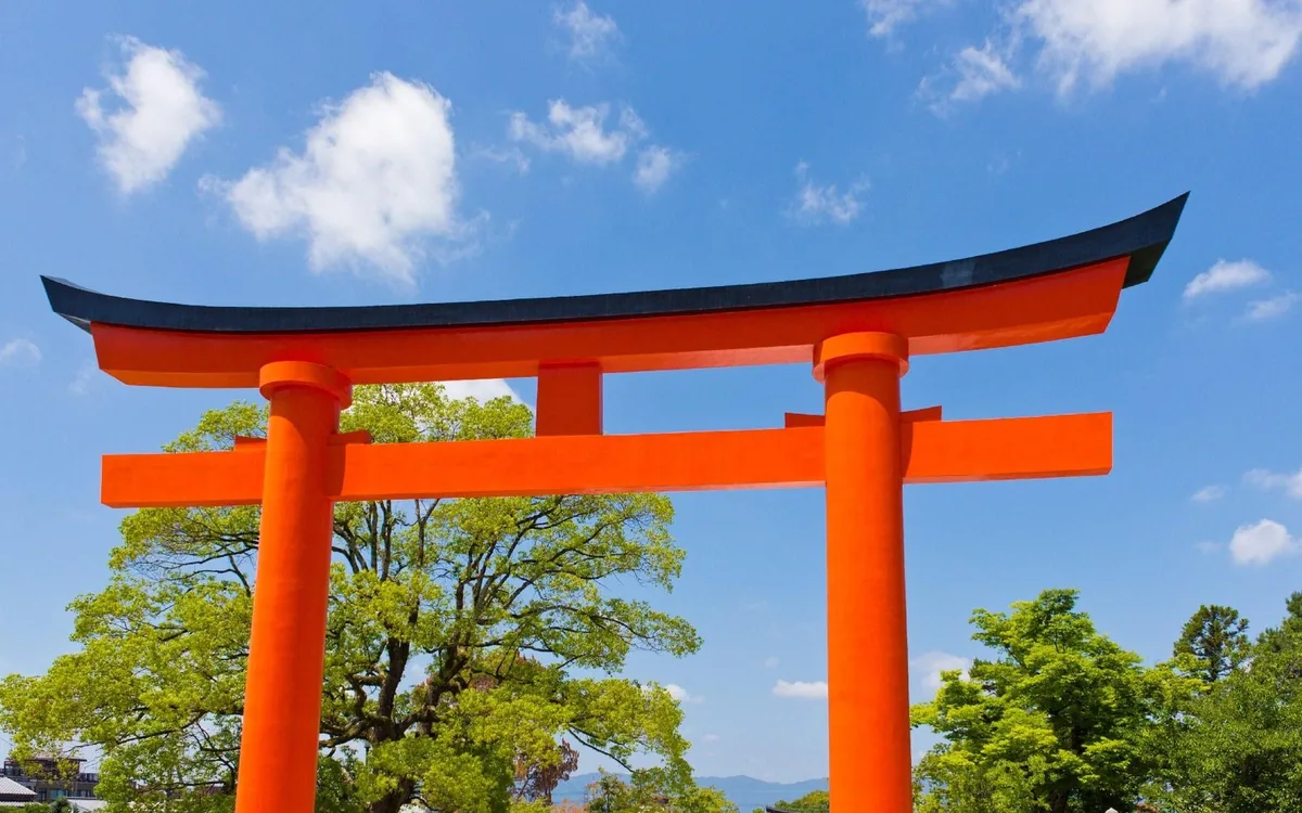 Ein großes zinnoberrotes Torii-Tor vor blauem Himmel am Fushimi Inari Taisha in Kyoto